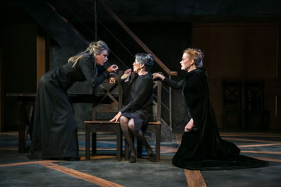 All the women in black dresses and clocks, Margaret leaning over and gesturing in the face of the Duchess of York sitting on a chair as Elizabeth kneels next to her.